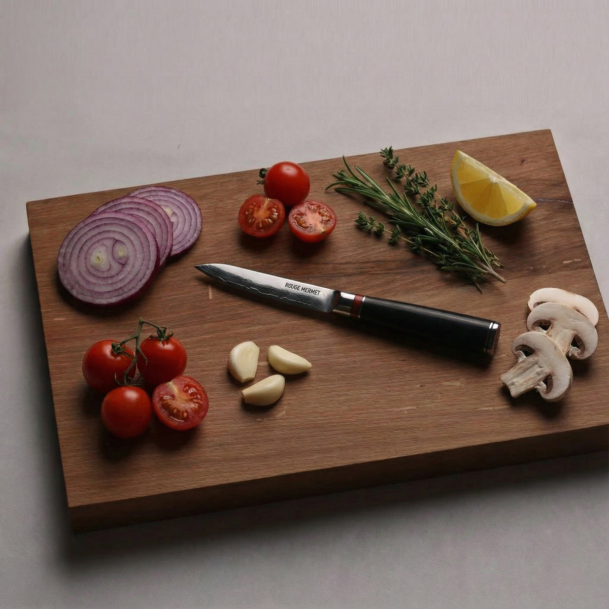 Couteau d’office Rouge Mermet sur une planche en bois avec tomates, ail et champignons