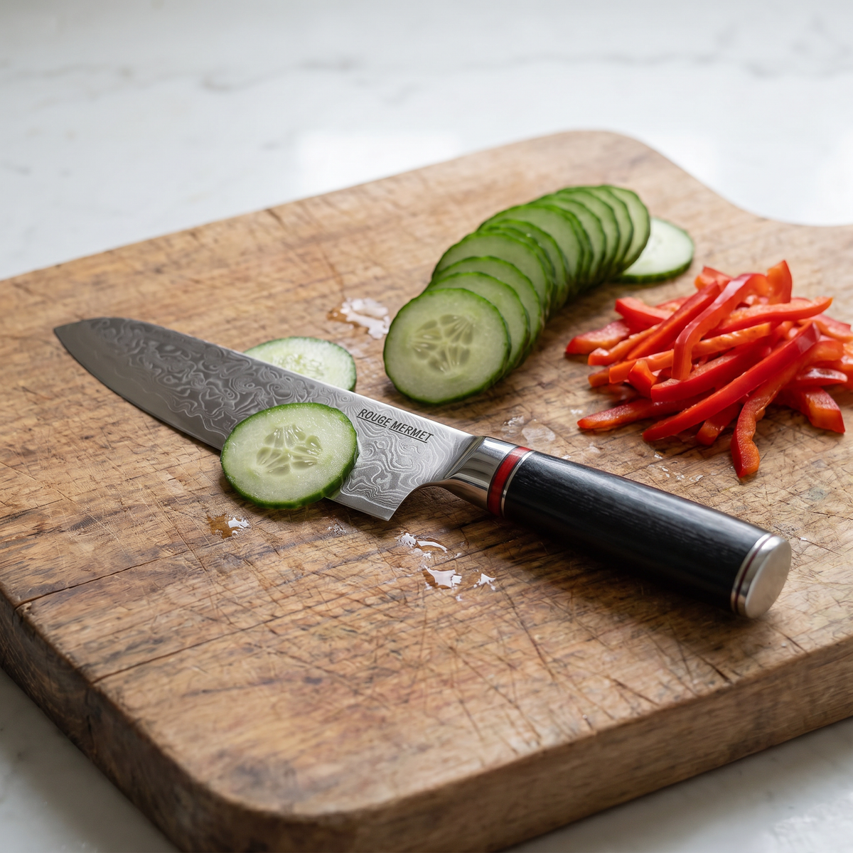 Couteau santoku Rouge Mermet sur une planche en bois, après avoir émincé un concombre et un poivron rouge