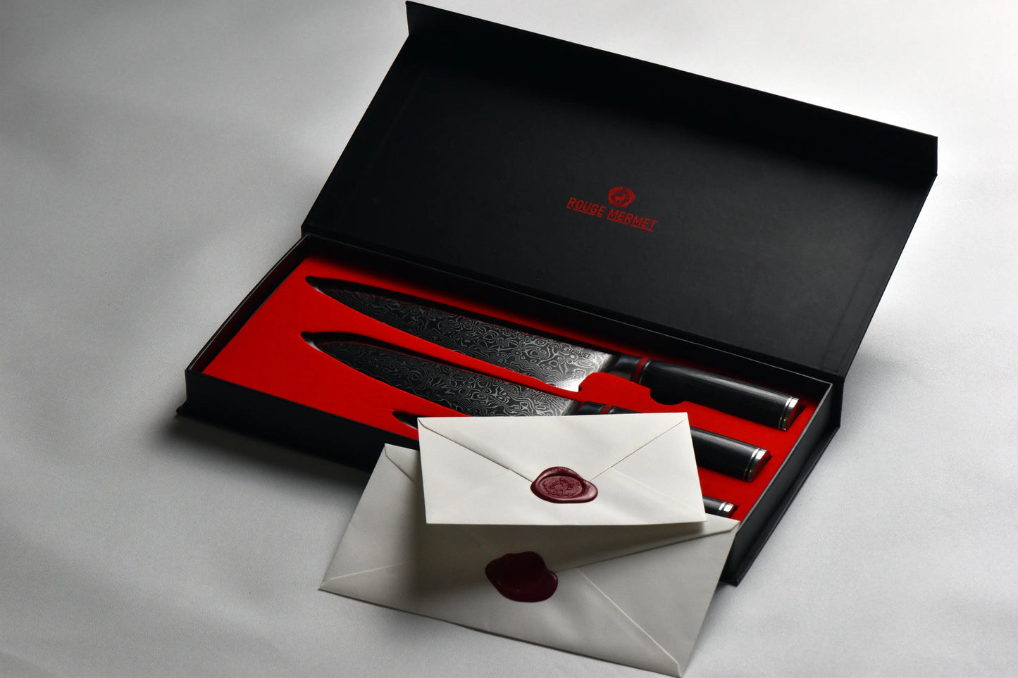 boite de 3 couteaux de cuisine. La boite est noire avec une mousse rouge. Il y à un fond blanc et les enveloppes dans lesquelles on trouve le certificat d'authenticité.