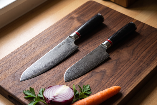 Couteau de chef et santoku Rouge Mermet en acier Damas VG10 côte à côte sur une planche en noyer, avec oignon rouge, carotte et persil