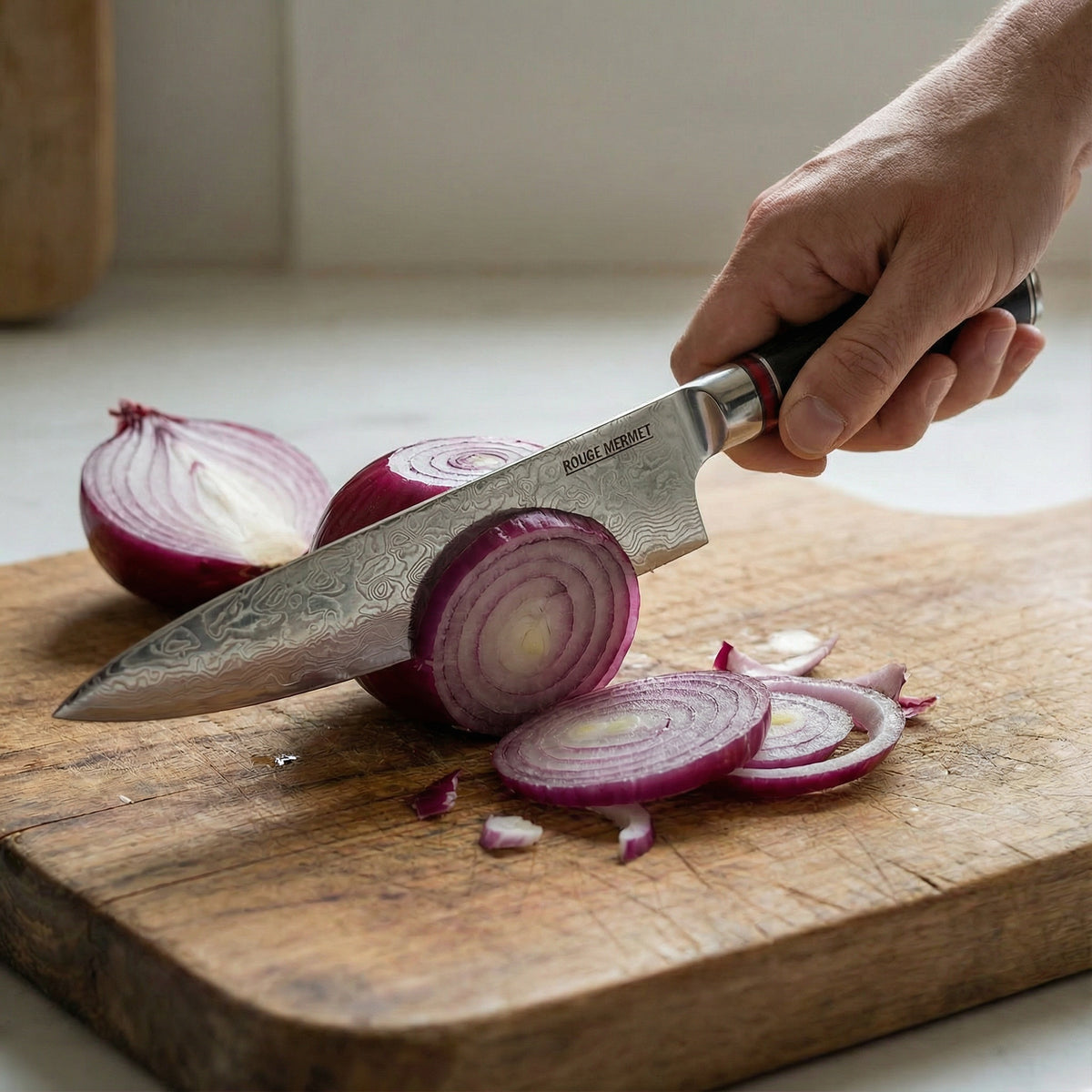 Couteau de chef Rouge Mermet en main, tranchant un oignon rouge sur une planche en bois