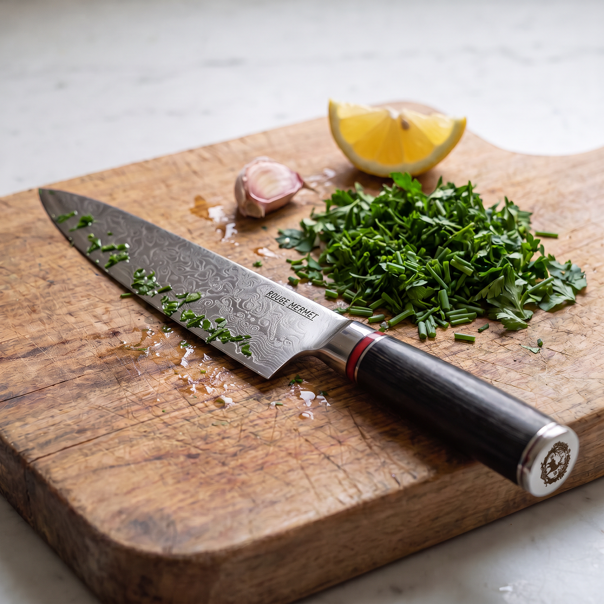 Couteau de chef Rouge Mermet sur une planche en bois, après avoir ciselé du persil et de la ciboulette